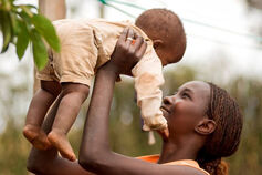 A woman smiles as she raises a small child above her head.